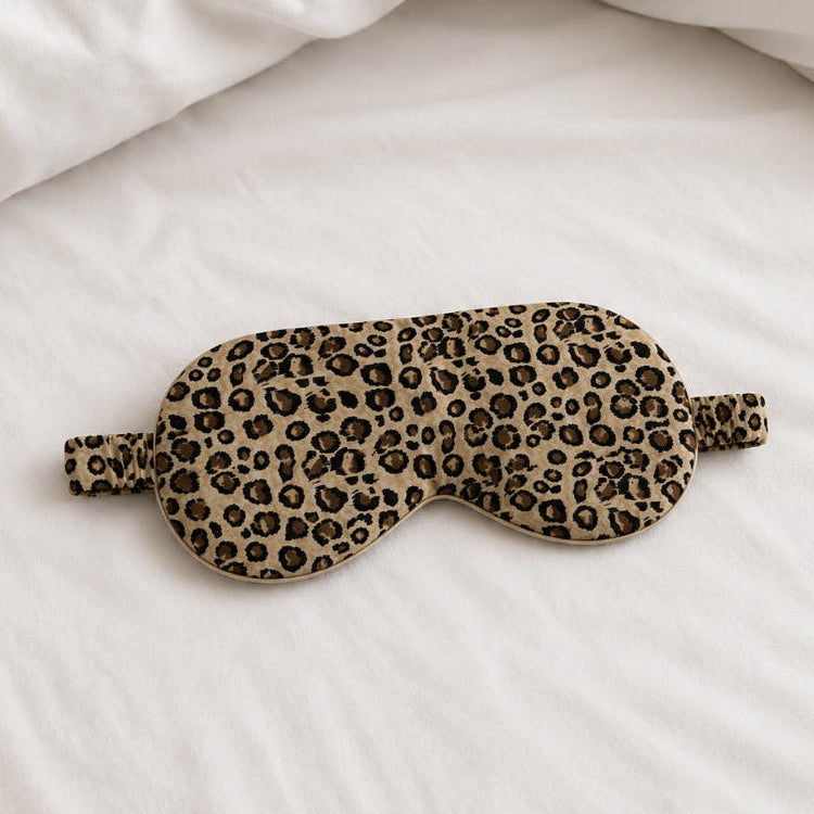 Jedwabna maska do spania Leopard z 100% jedwabiu morwowego 22 momme marki Lumière na białej satynowej pościeli.